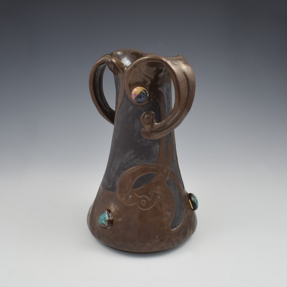 An Art Nouveau brown ceramic vase featuring a metallic copper effect surface, organic twin handles, flared rim, and inset colourful glazed cabochons. View VI