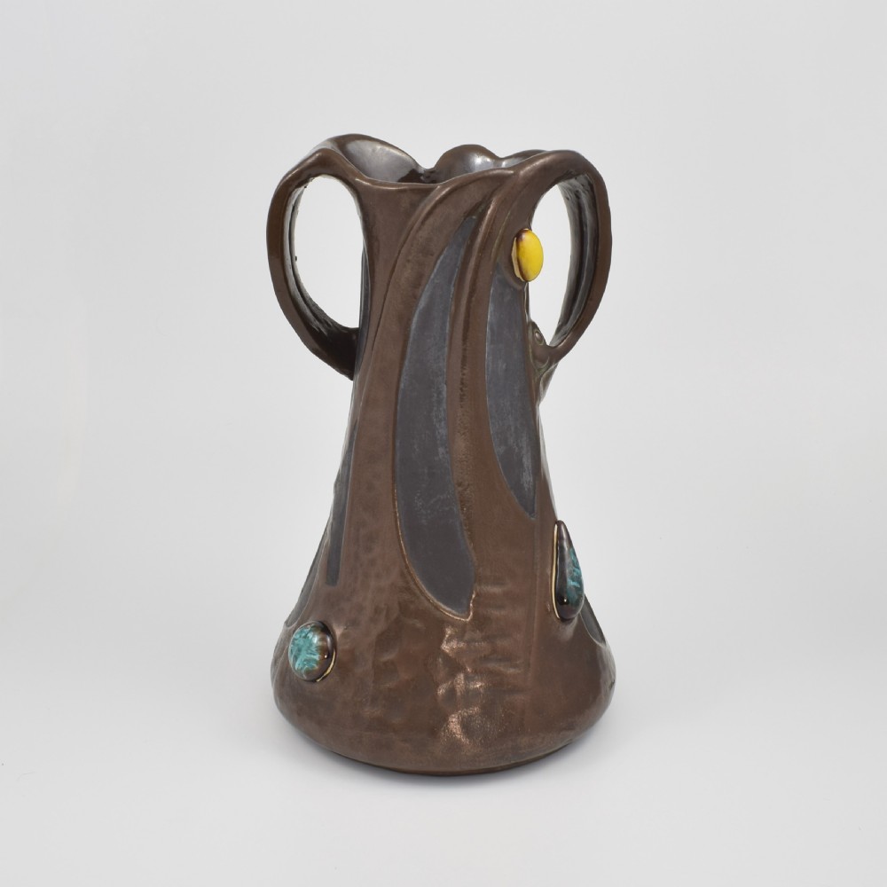 An Art Nouveau brown ceramic vase featuring a metallic copper effect surface, organic twin handles, flared rim, and inset colourful glazed cabochons. View XVI