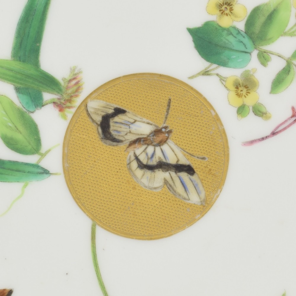 A circular cream porcelain dessert plate decorated with a central gilded sun motif, hand-painted butterflies, botanical sprigs, and a gilded rim. View III
