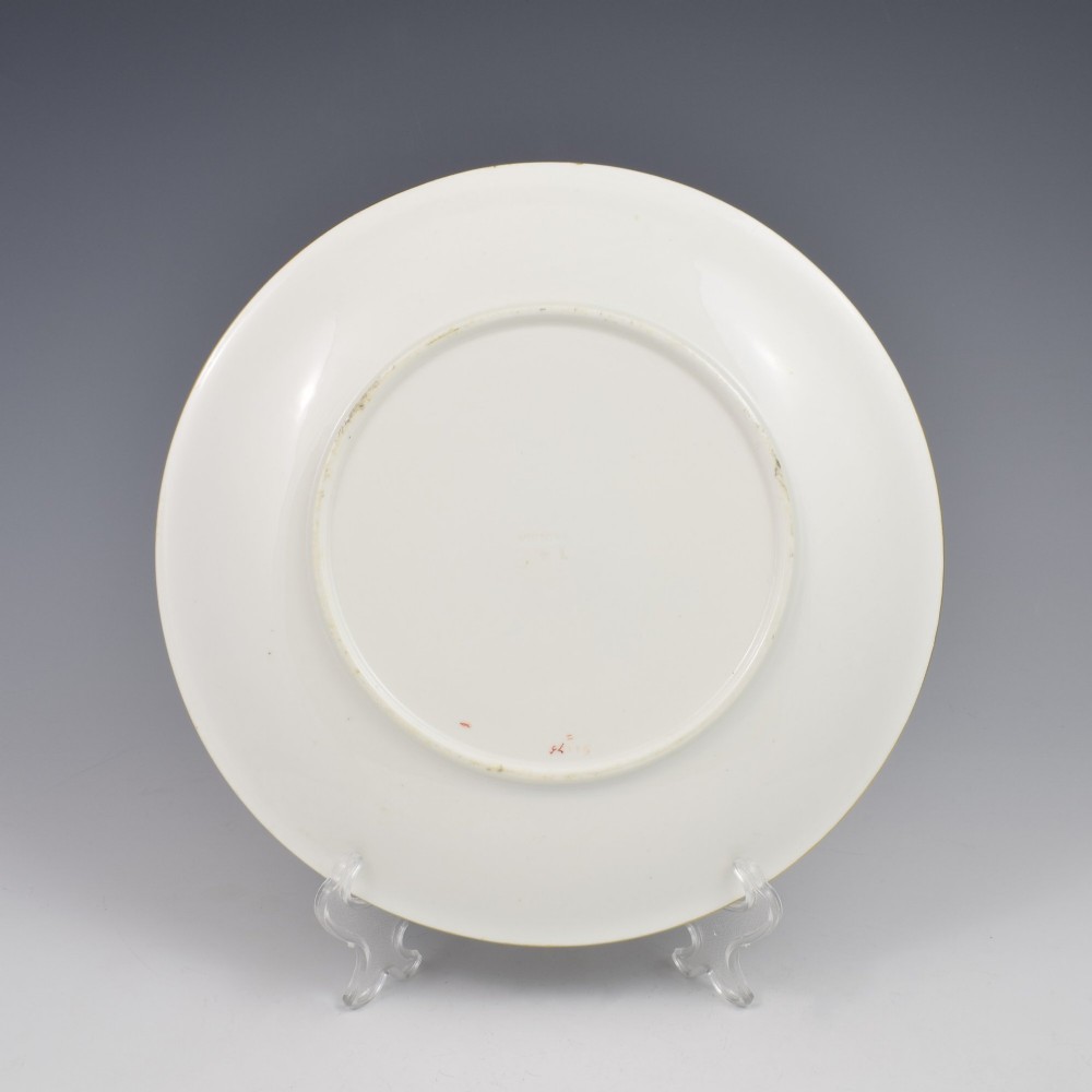 A circular cream porcelain dessert plate decorated with a central gilded sun motif, hand-painted butterflies, botanical sprigs, and a gilded rim. View V