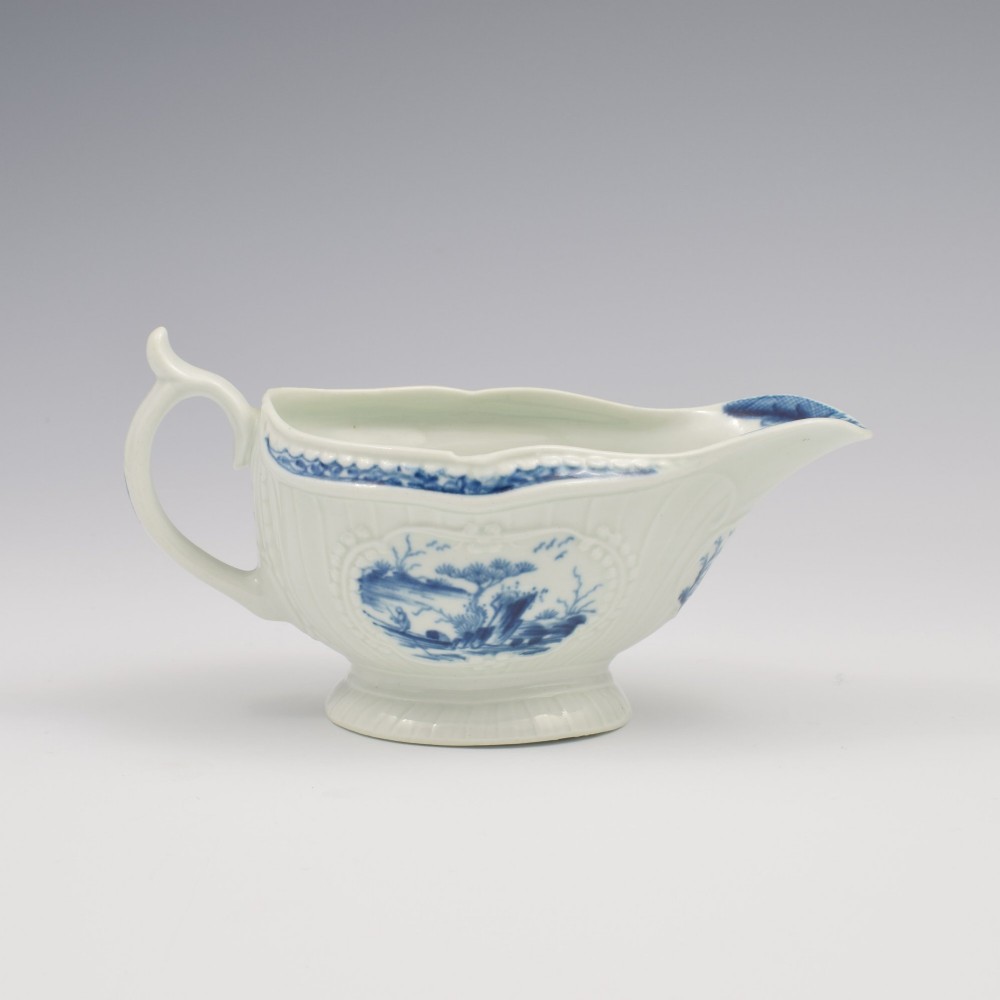 An eighteenth-century blue and white soft-paste porcelain sauce boat with a moulded fluted body, scroll handle, and underglaze blue landscape decoration.