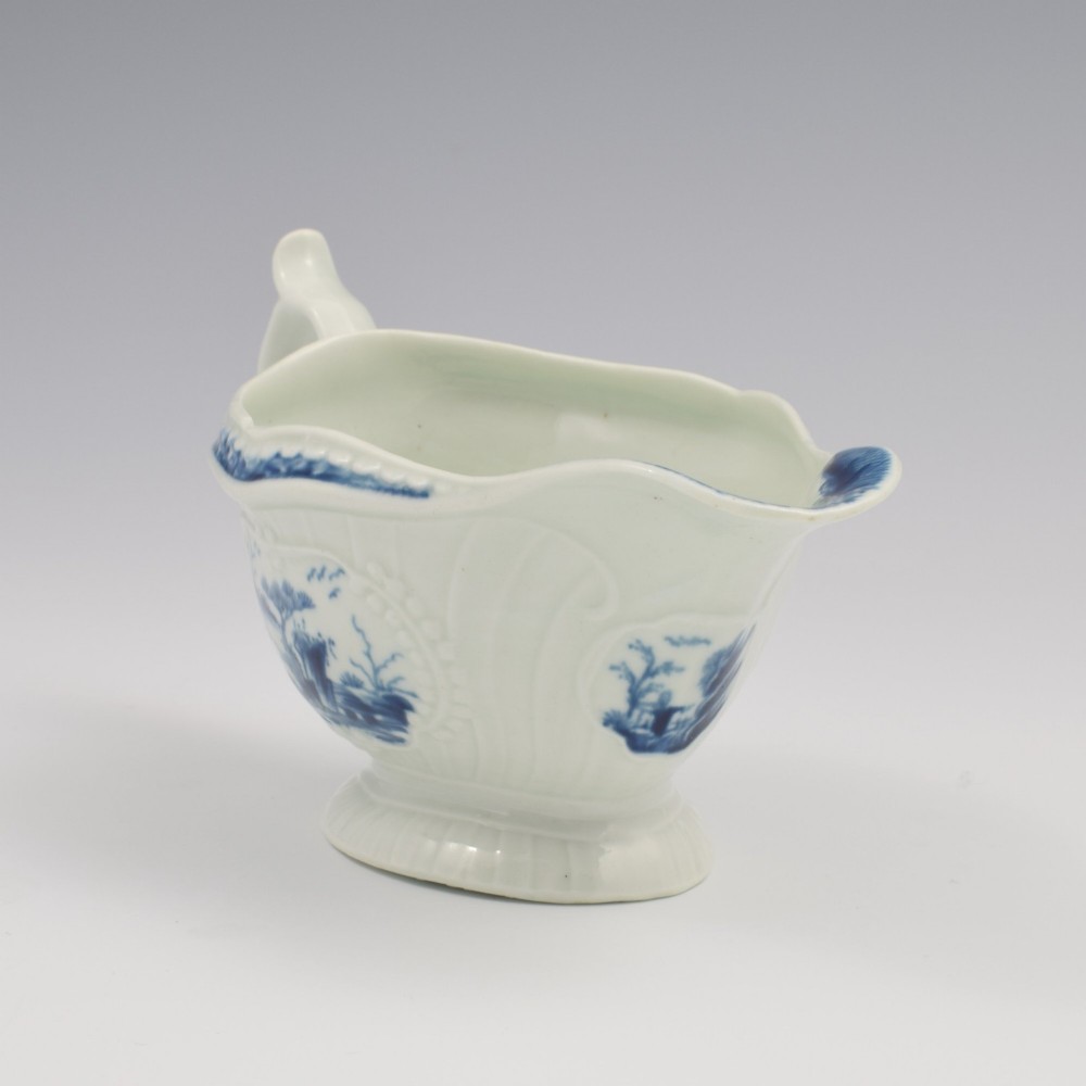 An eighteenth-century blue and white soft-paste porcelain sauce boat with a moulded fluted body, scroll handle, and underglaze blue landscape decoration. View II
