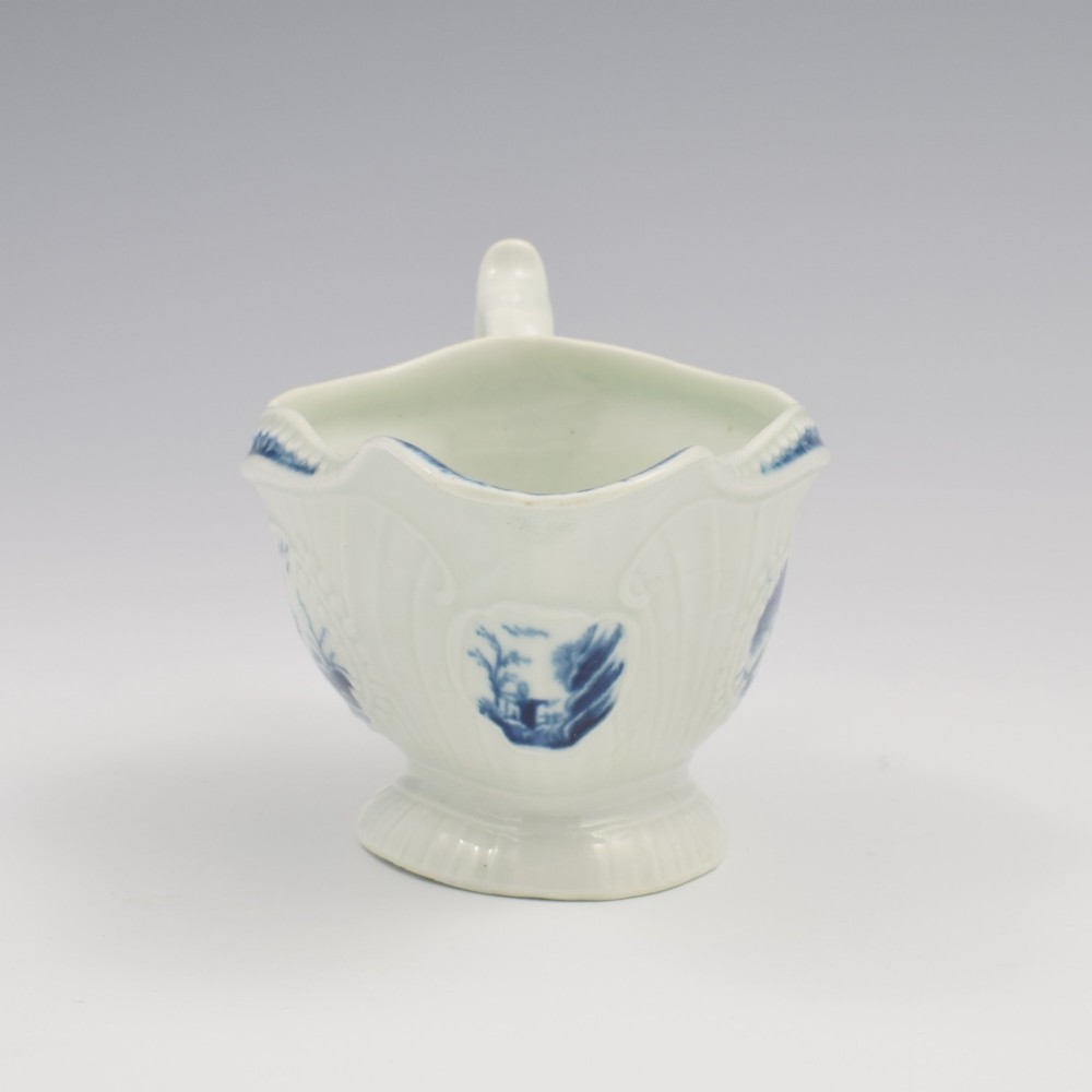 An eighteenth-century blue and white soft-paste porcelain sauce boat with a moulded fluted body, scroll handle, and underglaze blue landscape decoration. View III