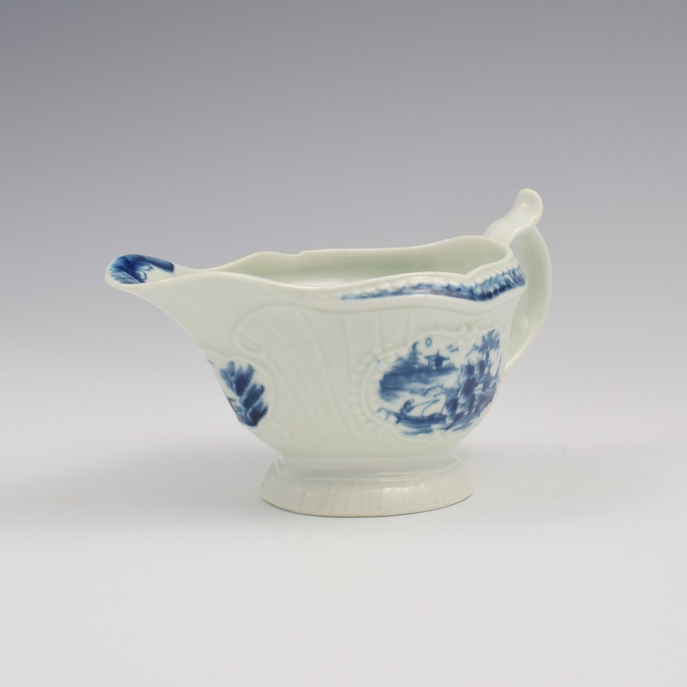 An eighteenth-century blue and white soft-paste porcelain sauce boat with a moulded fluted body, scroll handle, and underglaze blue landscape decoration. View IV