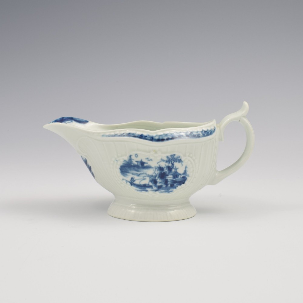 An eighteenth-century blue and white soft-paste porcelain sauce boat with a moulded fluted body, scroll handle, and underglaze blue landscape decoration. View V