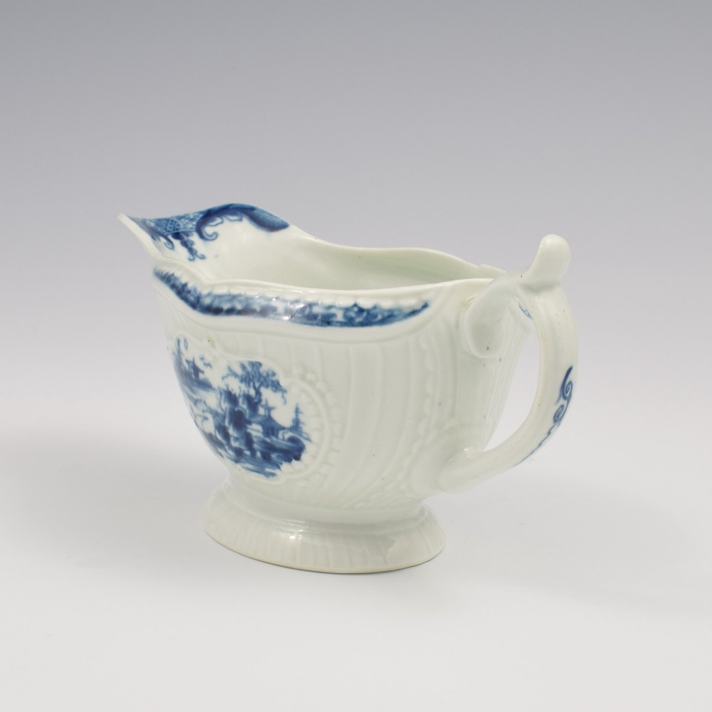 An eighteenth-century blue and white soft-paste porcelain sauce boat with a moulded fluted body, scroll handle, and underglaze blue landscape decoration. View VI