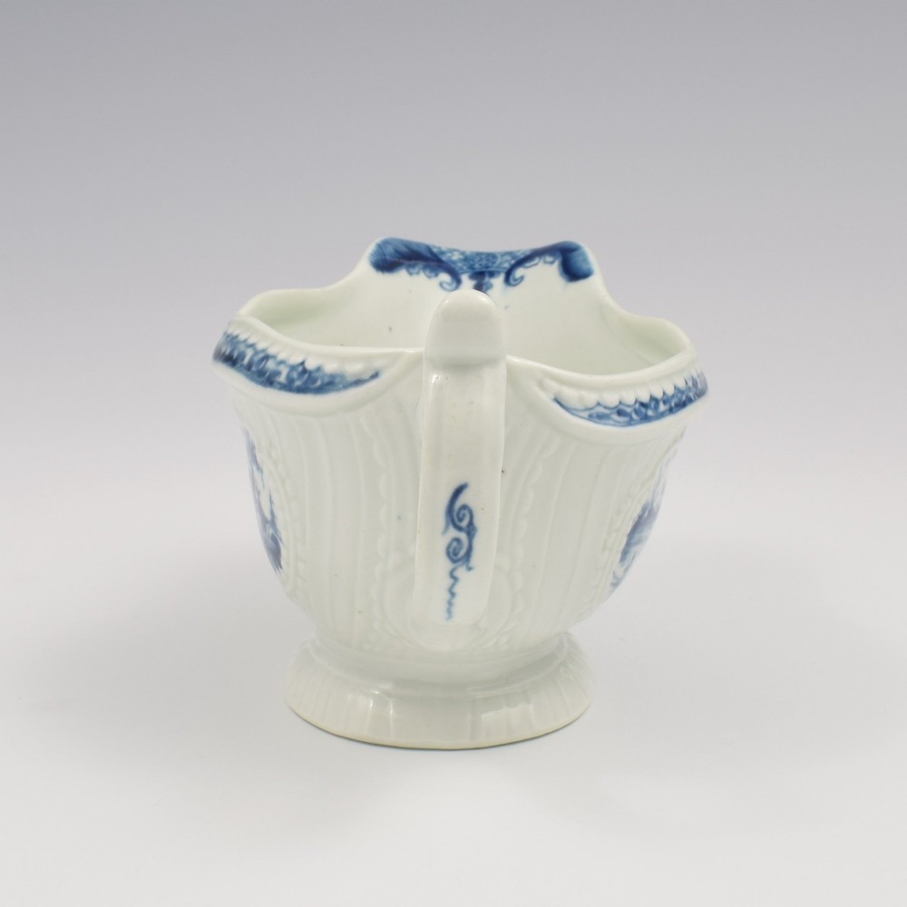 An eighteenth-century blue and white soft-paste porcelain sauce boat with a moulded fluted body, scroll handle, and underglaze blue landscape decoration. View VII