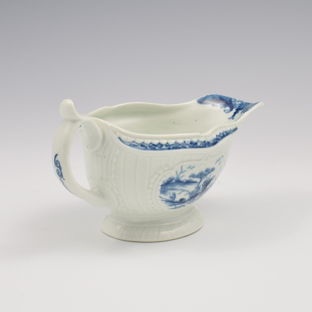An eighteenth-century blue and white soft-paste porcelain sauce boat with a moulded fluted body, scroll handle, and underglaze blue landscape decoration. View VIII