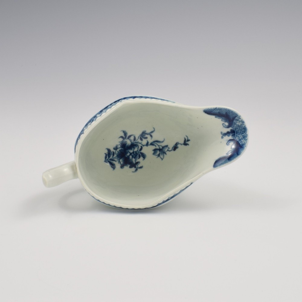An eighteenth-century blue and white soft-paste porcelain sauce boat with a moulded fluted body, scroll handle, and underglaze blue landscape decoration. View IX