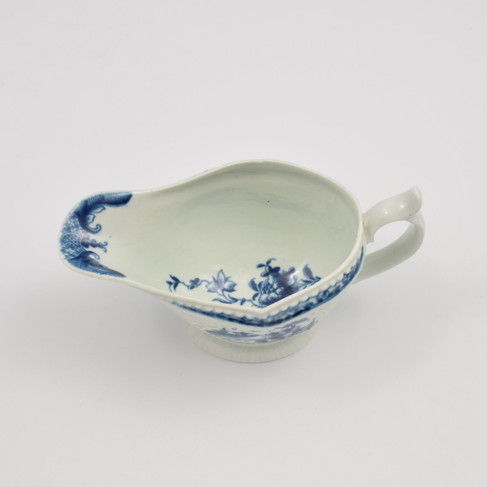 An eighteenth-century blue and white soft-paste porcelain sauce boat with a moulded fluted body, scroll handle, and underglaze blue landscape decoration. View XI