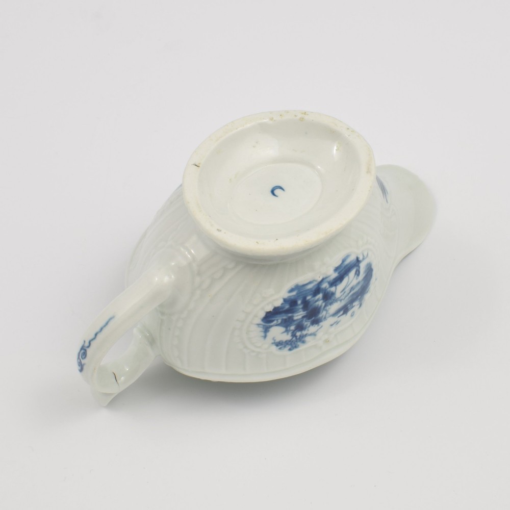 An eighteenth-century blue and white soft-paste porcelain sauce boat with a moulded fluted body, scroll handle, and underglaze blue landscape decoration. View XII
