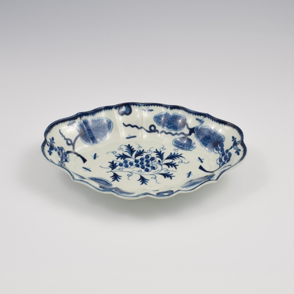 An oval 18th-century soft-paste porcelain dessert dish featuring a lobed rim decorated with underglaze cobalt blue foliage and botanical motifs on a white background. View III