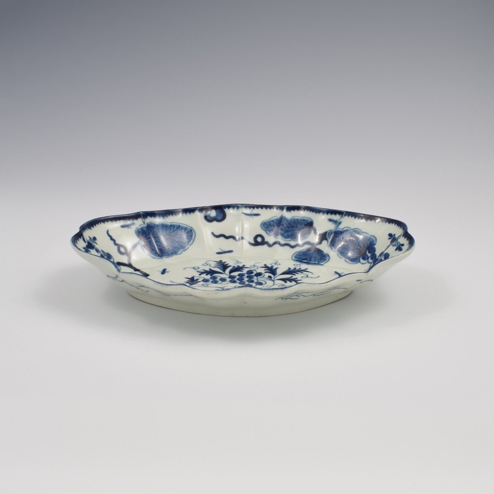 An oval 18th-century soft-paste porcelain dessert dish featuring a lobed rim decorated with underglaze cobalt blue foliage and botanical motifs on a white background. View IV