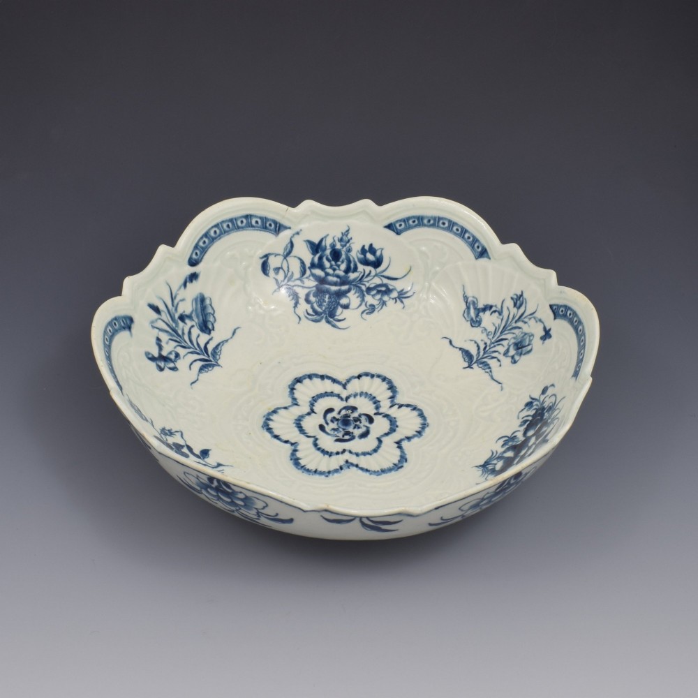 An eighteenth-century circular soft-paste porcelain junket dish featuring a scalloped rim, relief shell moulding, and painted blue floral motifs.