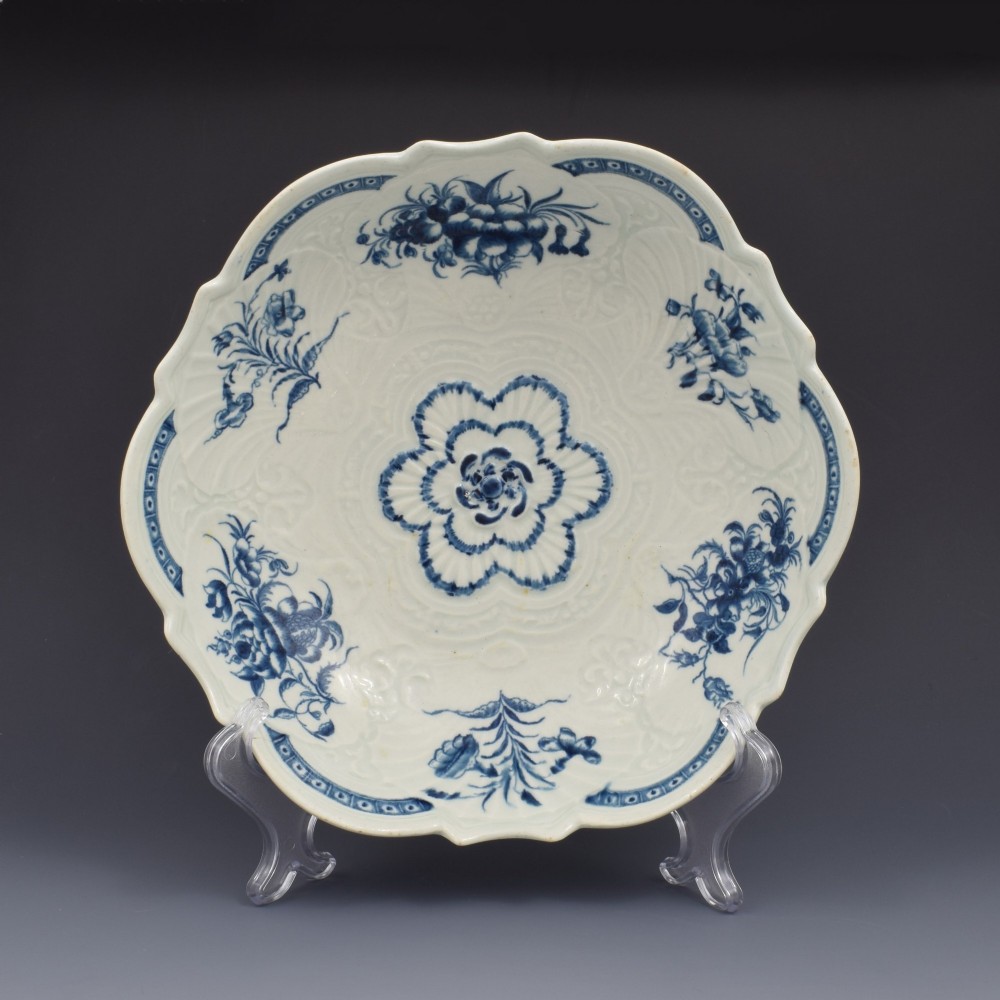 An eighteenth-century circular soft-paste porcelain junket dish featuring a scalloped rim, relief shell moulding, and painted blue floral motifs. View II