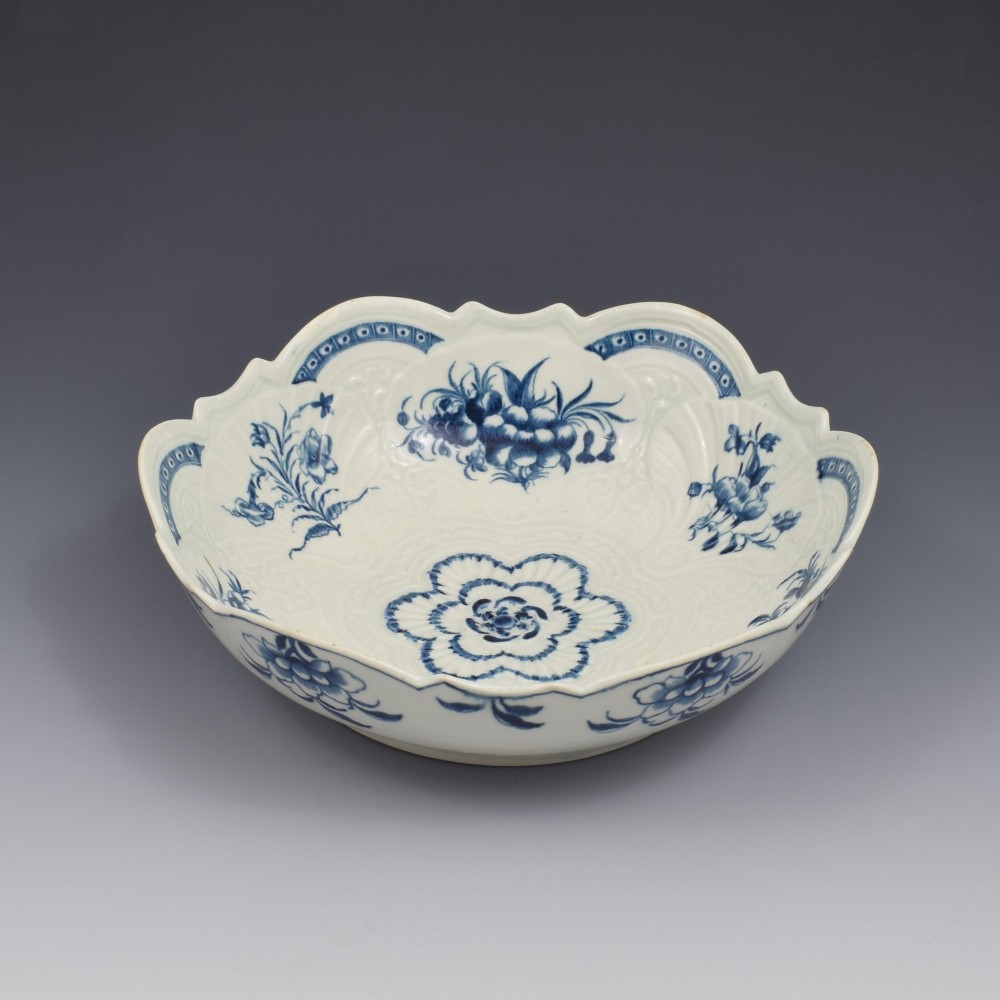 An eighteenth-century circular soft-paste porcelain junket dish featuring a scalloped rim, relief shell moulding, and painted blue floral motifs. View III