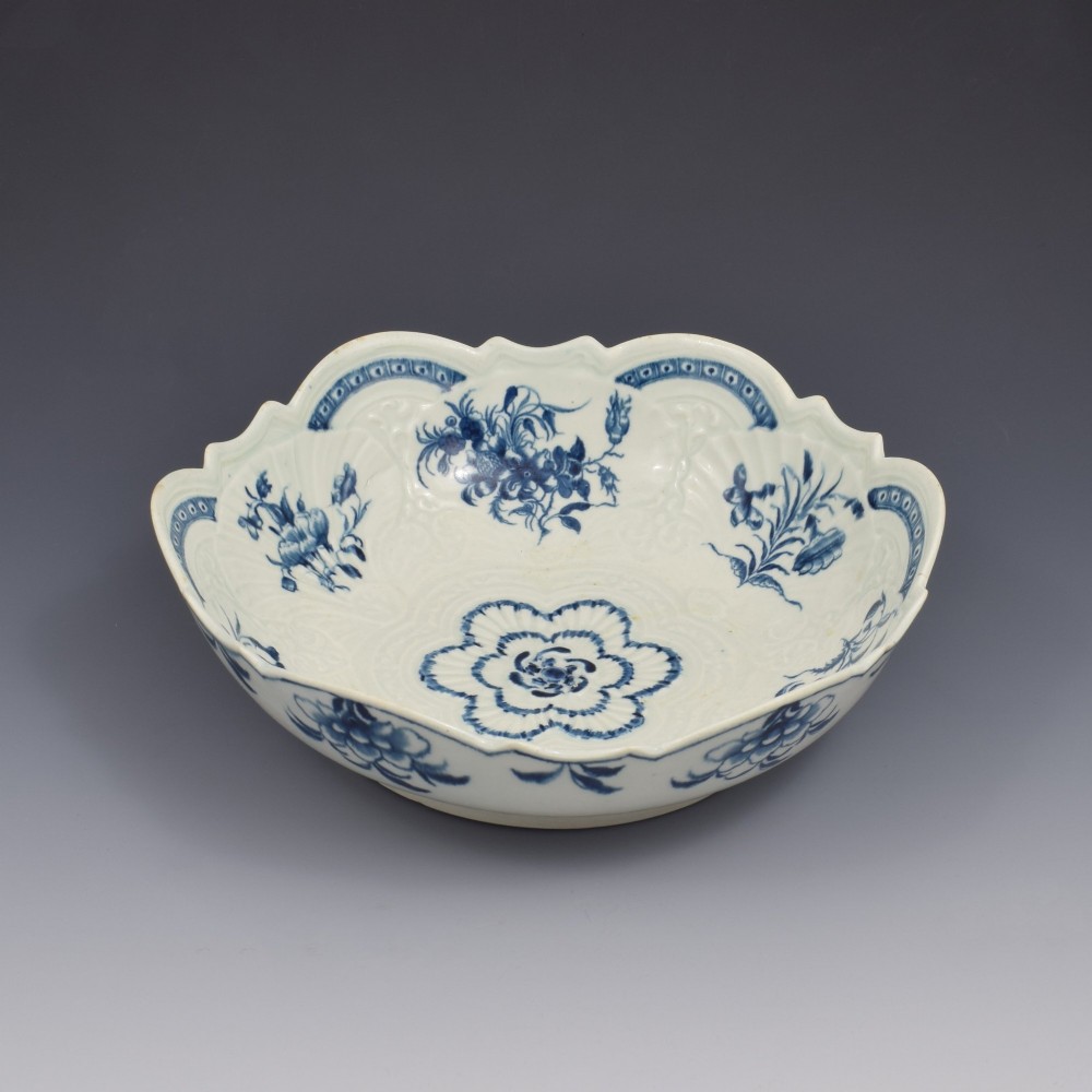 An eighteenth-century circular soft-paste porcelain junket dish featuring a scalloped rim, relief shell moulding, and painted blue floral motifs. View IV