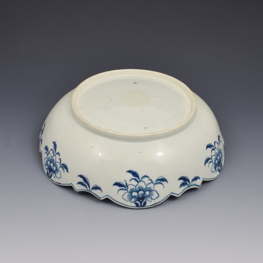 An eighteenth-century circular soft-paste porcelain junket dish featuring a scalloped rim, relief shell moulding, and painted blue floral motifs. View VII