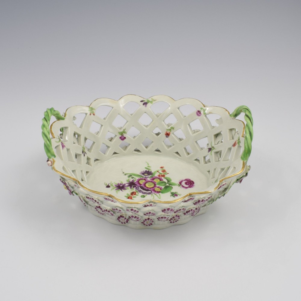 An eighteenth-century reticulated soft-paste porcelain chestnut basket featuring pierced lattice sides, green twig handles, and hand-painted polychrome floral decoration.