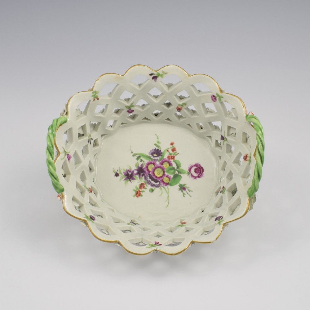 An eighteenth-century reticulated soft-paste porcelain chestnut basket featuring pierced lattice sides, green twig handles, and hand-painted polychrome floral decoration. View II