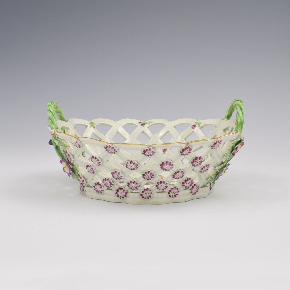 An eighteenth-century reticulated soft-paste porcelain chestnut basket featuring pierced lattice sides, green twig handles, and hand-painted polychrome floral decoration. View III