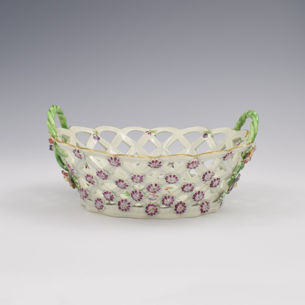 An eighteenth-century reticulated soft-paste porcelain chestnut basket featuring pierced lattice sides, green twig handles, and hand-painted polychrome floral decoration. View V