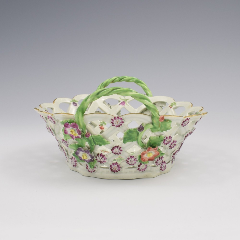 An eighteenth-century reticulated soft-paste porcelain chestnut basket featuring pierced lattice sides, green twig handles, and hand-painted polychrome floral decoration. View VI
