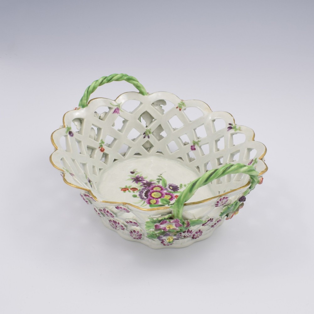 An eighteenth-century reticulated soft-paste porcelain chestnut basket featuring pierced lattice sides, green twig handles, and hand-painted polychrome floral decoration. View VII