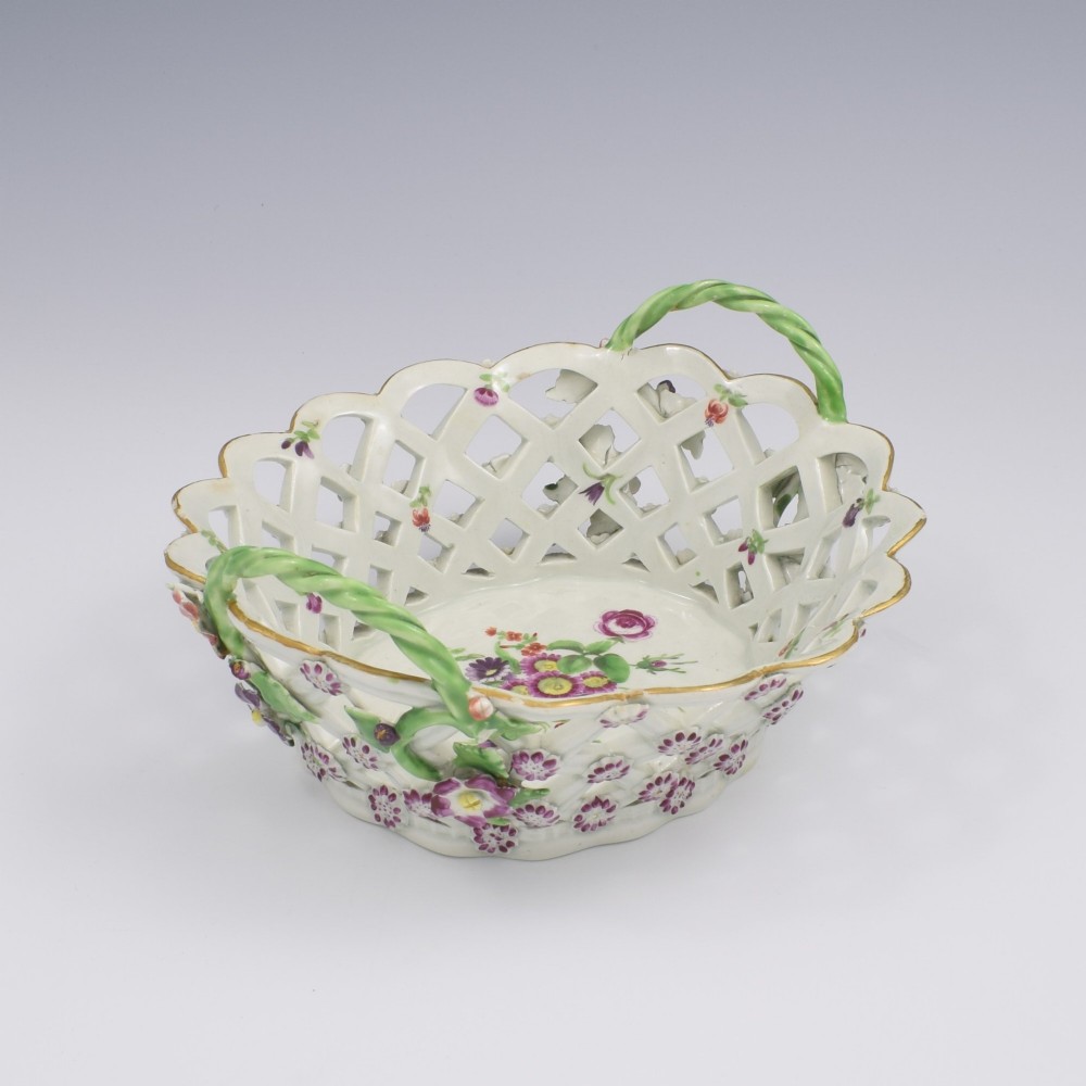 An eighteenth-century reticulated soft-paste porcelain chestnut basket featuring pierced lattice sides, green twig handles, and hand-painted polychrome floral decoration. View VIII