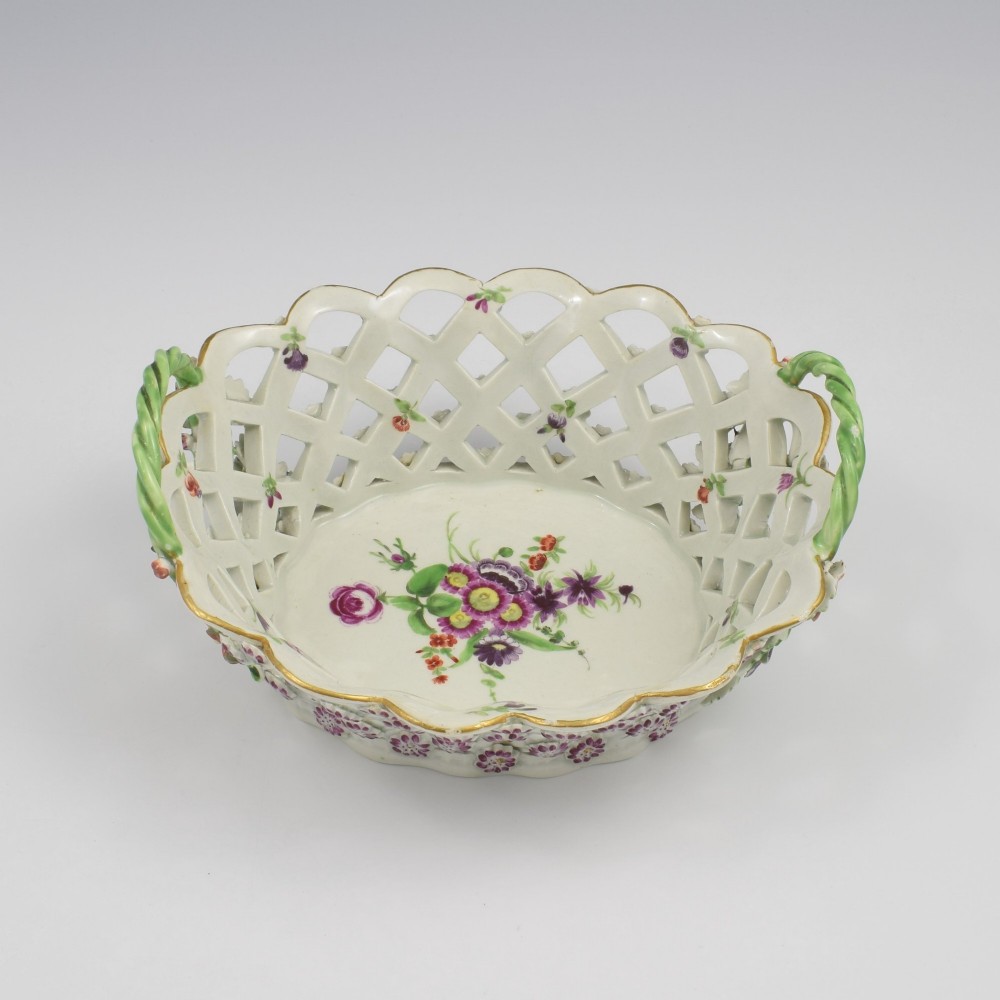 An eighteenth-century reticulated soft-paste porcelain chestnut basket featuring pierced lattice sides, green twig handles, and hand-painted polychrome floral decoration. View IX