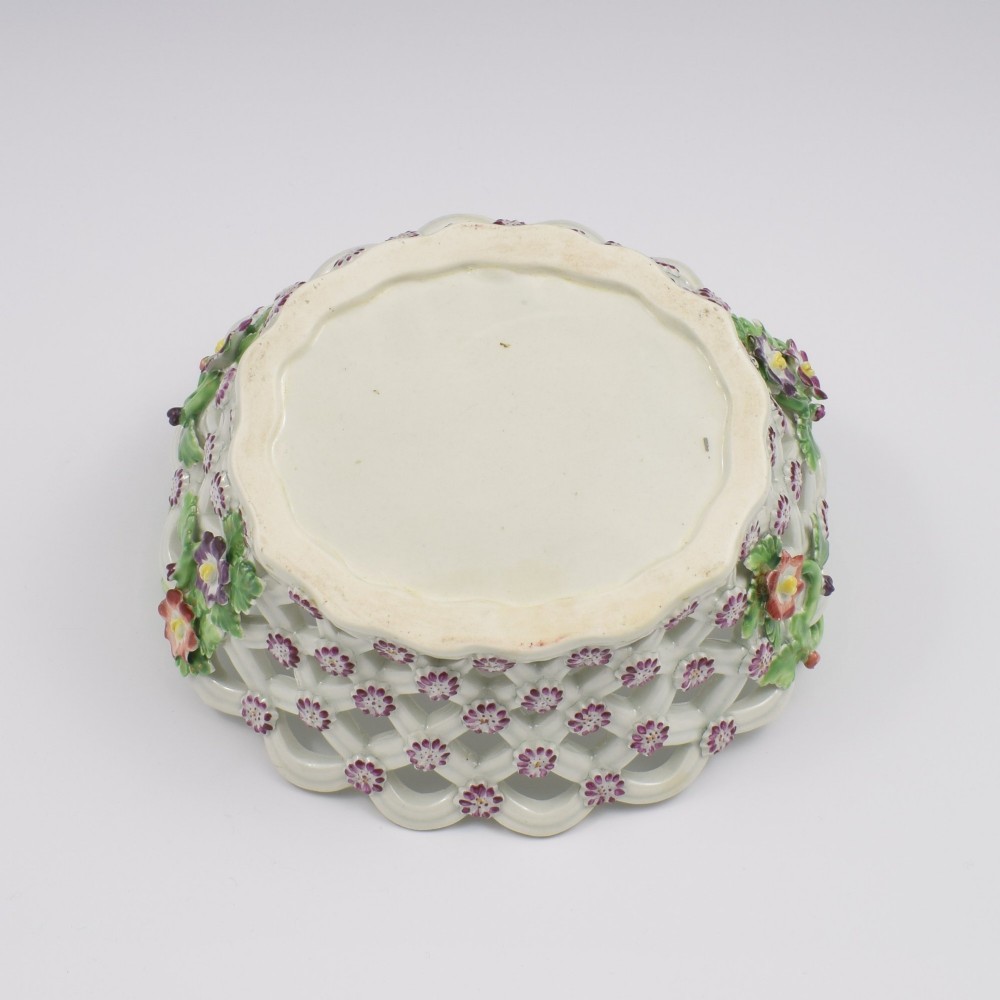 An eighteenth-century reticulated soft-paste porcelain chestnut basket featuring pierced lattice sides, green twig handles, and hand-painted polychrome floral decoration. View X