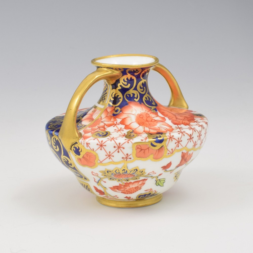 An Edwardian Royal Crown Derby miniature twin-handled porcelain vase decorated with an Imari floral pattern in cobalt blue, iron red, and gilt. View VI