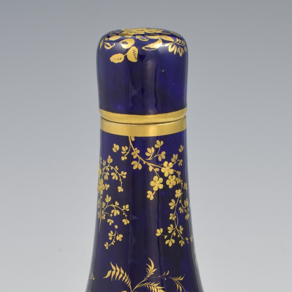 A cobalt blue porcelain bottle vase decorated with elaborate gold floral gilding and fitted with a matching rounded stopper. View VII