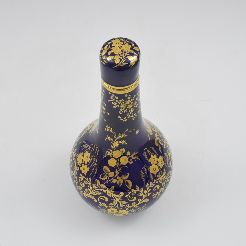 A cobalt blue porcelain bottle vase decorated with elaborate gold floral gilding and fitted with a matching rounded stopper. View X