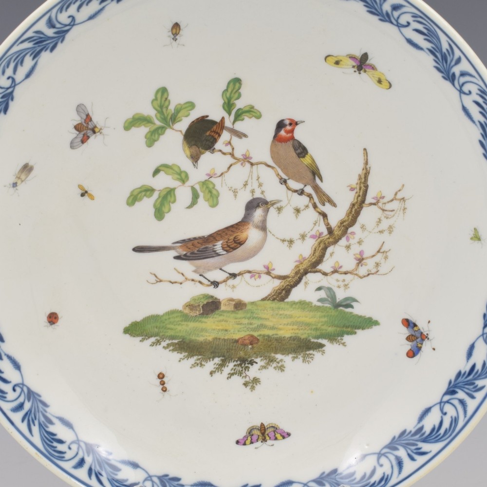 A circular white porcelain dish painted with detailed birds perched on a branch surrounded by small insects and framed by a blue foliate border. View II