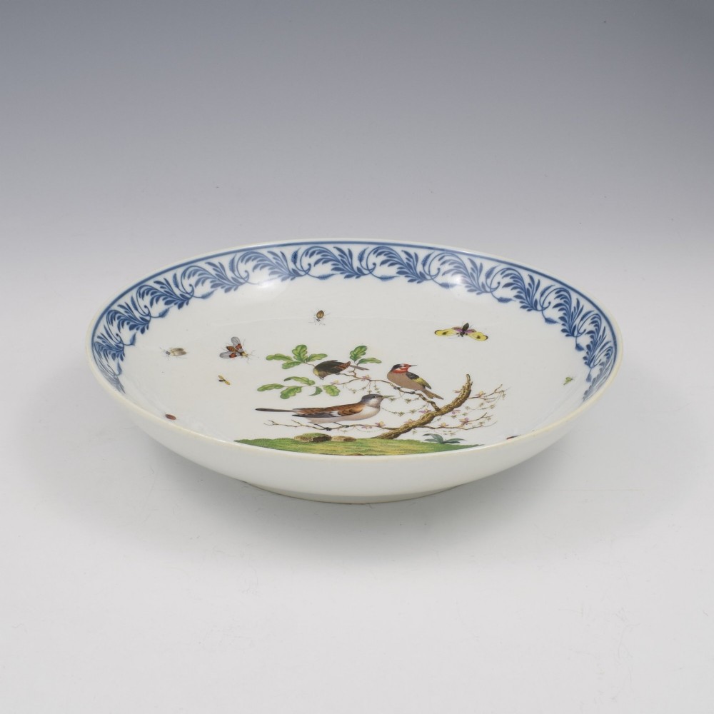 A circular white porcelain dish painted with detailed birds perched on a branch surrounded by small insects and framed by a blue foliate border. View V