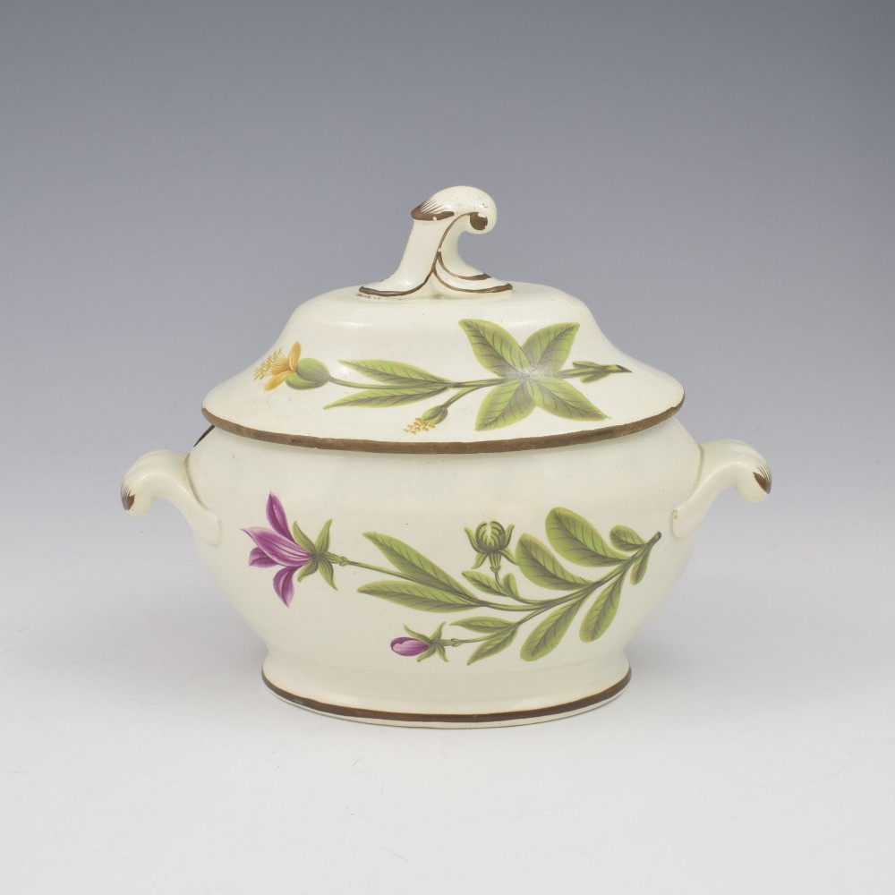 A Georgian cream pearlware lidded sauce tureen hand painted with botanical flowers and featuring scroll handles and a scroll finial.