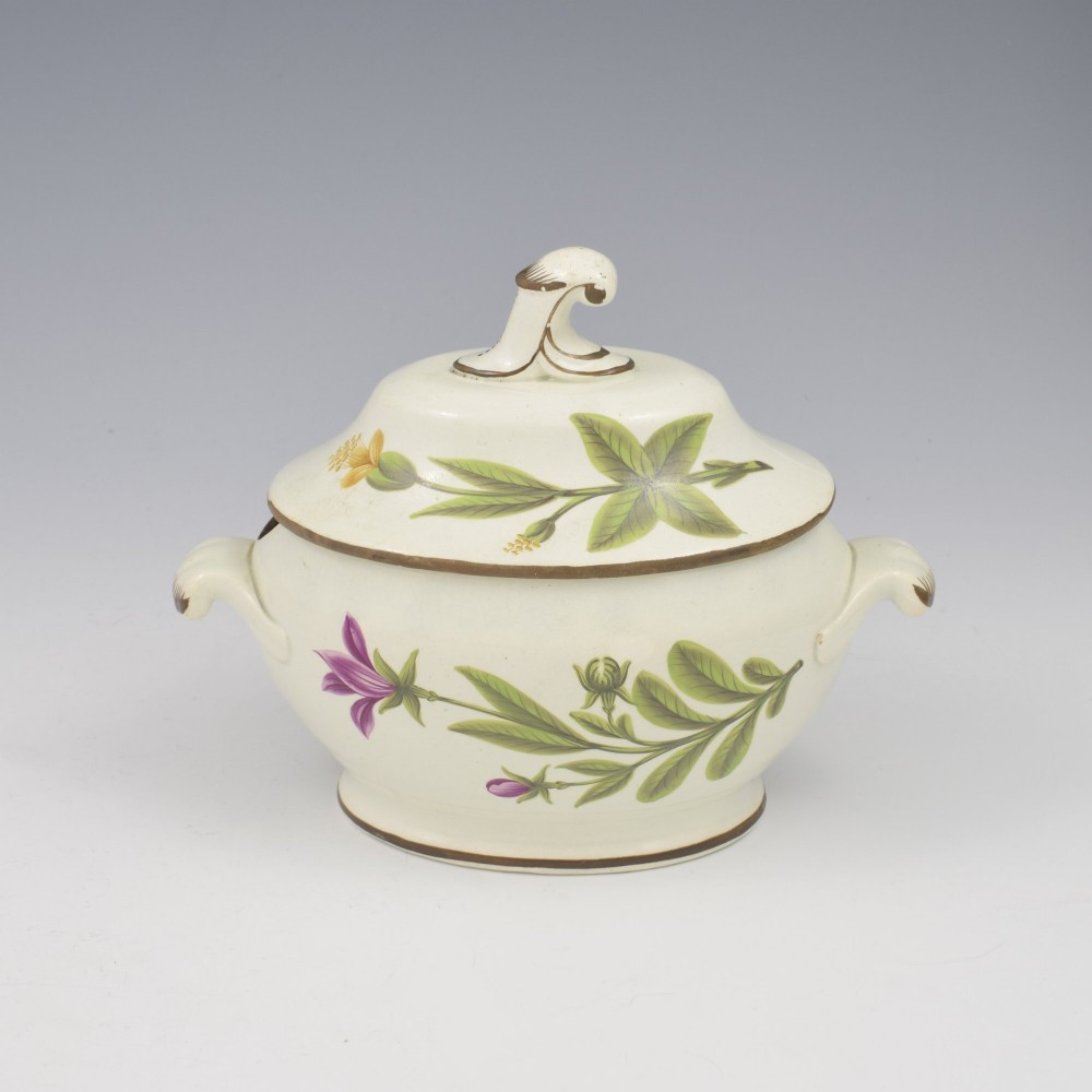 A Georgian cream pearlware lidded sauce tureen hand painted with botanical flowers and featuring scroll handles and a scroll finial. View II
