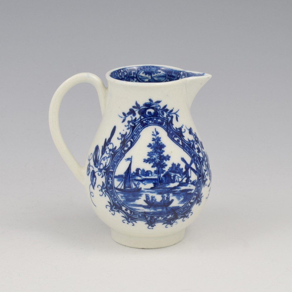 A Georgian blue and white soft-paste porcelain cream jug decorated with an underglaze landscape print in a cartouche frame.