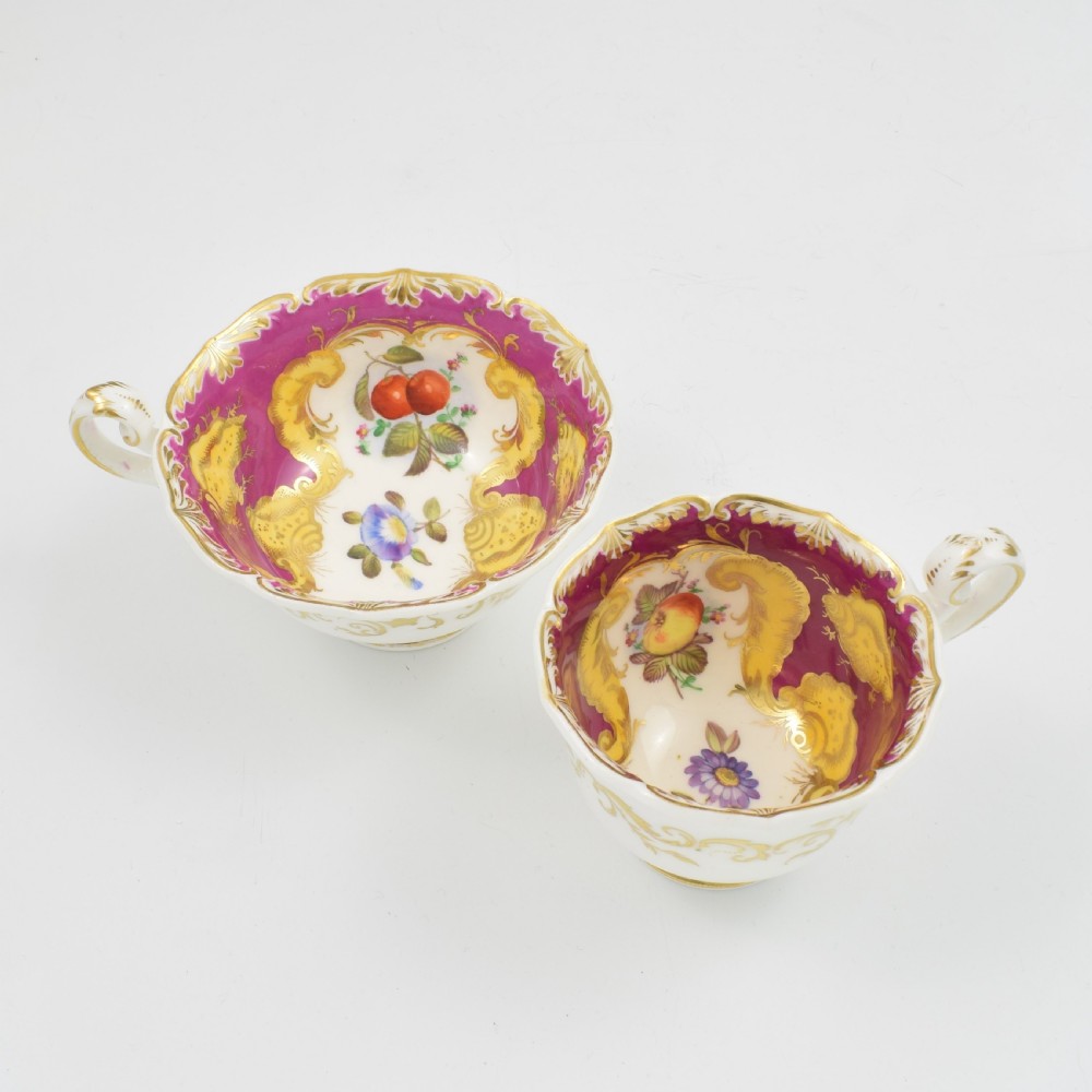 An antique English porcelain tea trio comprising a teacup, coffee cup, and saucer decorated with magenta ground, gilded scrollwork, and hand-painted fruit panels. View IV