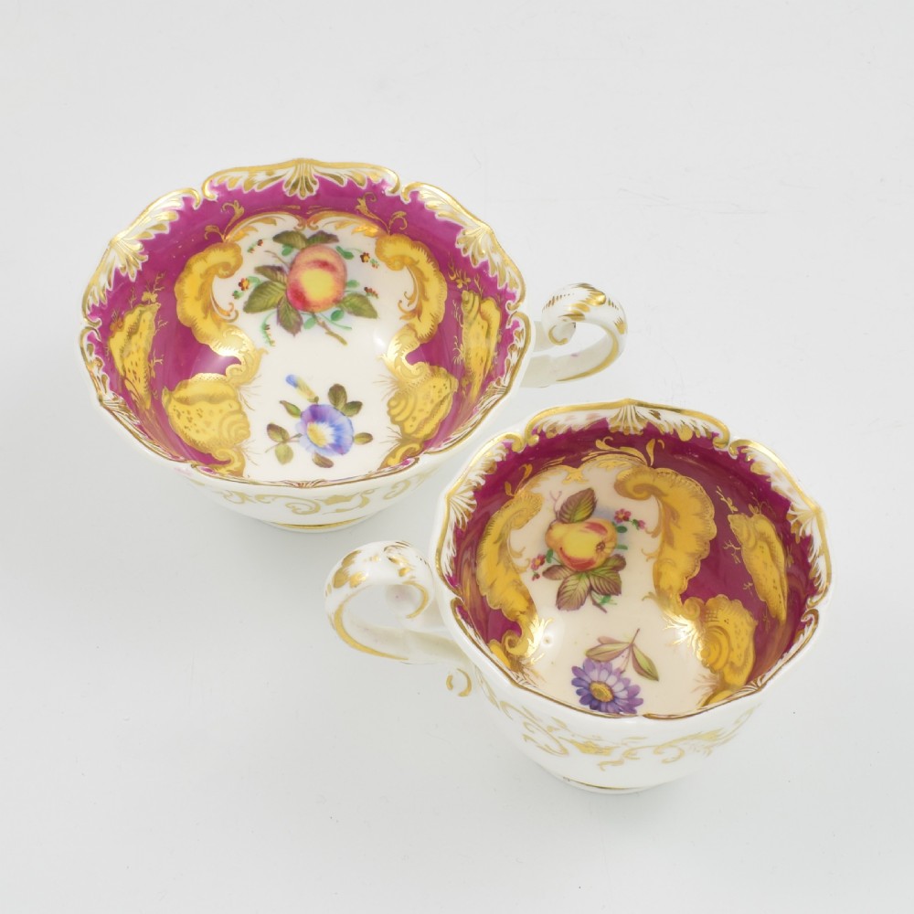 An antique English porcelain tea trio comprising a teacup, coffee cup, and saucer decorated with magenta ground, gilded scrollwork, and hand-painted fruit panels. View V