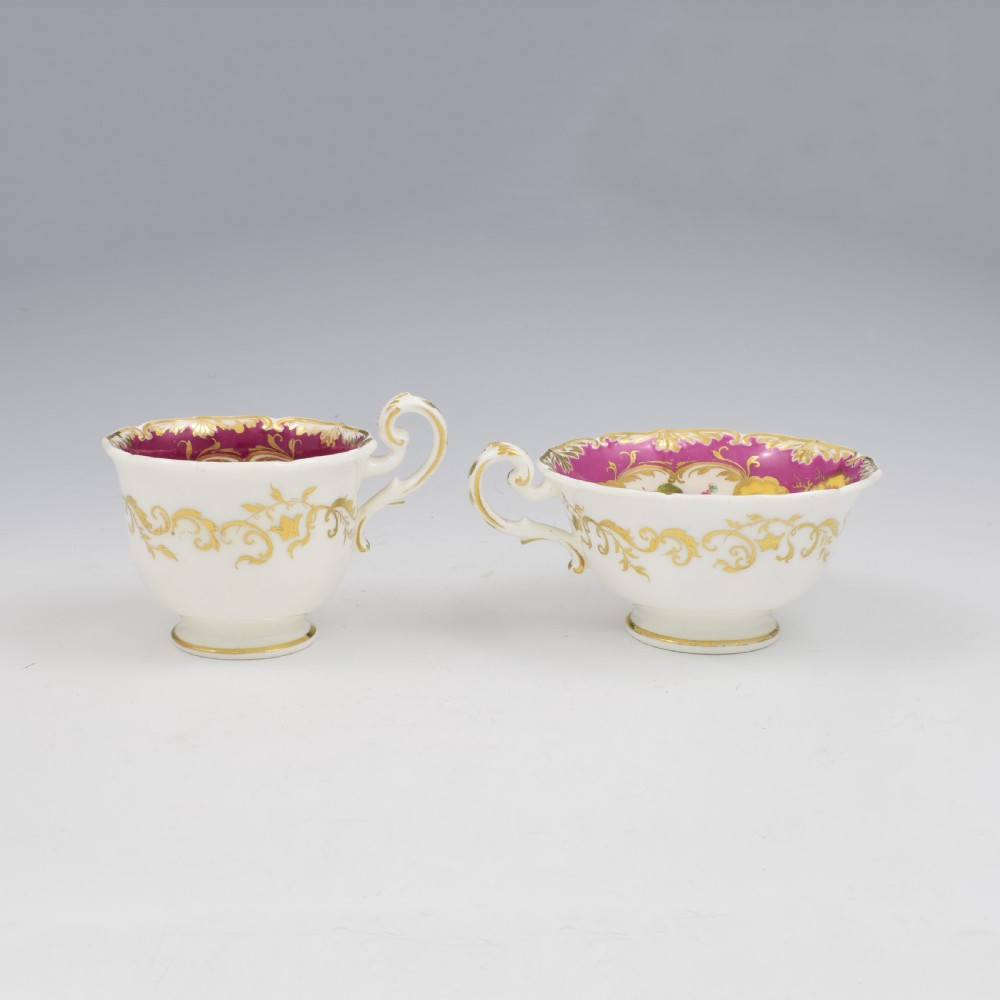 An antique English porcelain tea trio comprising a teacup, coffee cup, and saucer decorated with magenta ground, gilded scrollwork, and hand-painted fruit panels. View IX