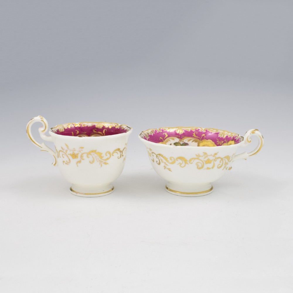 An antique English porcelain tea trio comprising a teacup, coffee cup, and saucer decorated with magenta ground, gilded scrollwork, and hand-painted fruit panels. View X