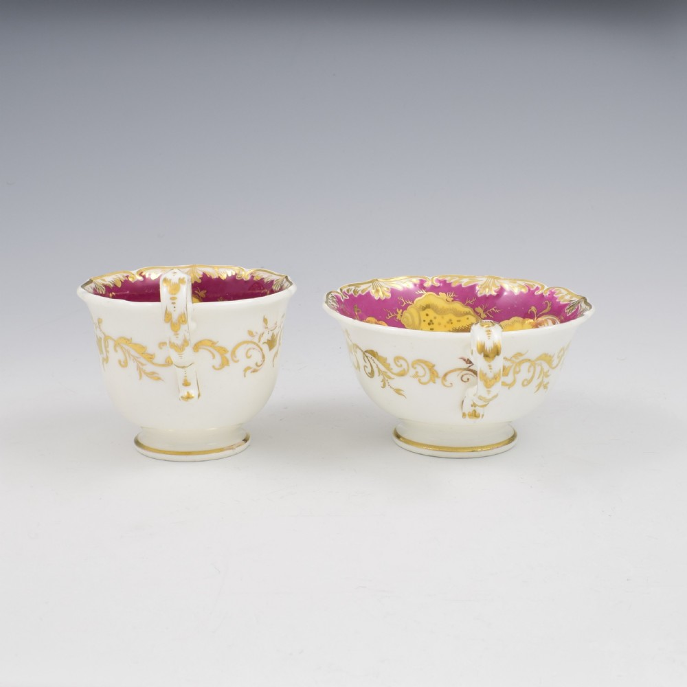An antique English porcelain tea trio comprising a teacup, coffee cup, and saucer decorated with magenta ground, gilded scrollwork, and hand-painted fruit panels. View XI