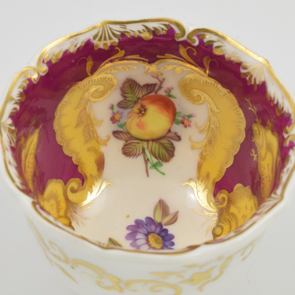 An antique English porcelain tea trio comprising a teacup, coffee cup, and saucer decorated with magenta ground, gilded scrollwork, and hand-painted fruit panels. View XII