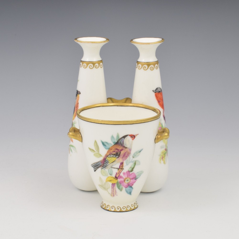 A Victorian white porcelain triple vase featuring three connected vessels decorated with hand-painted birds and gilt trim.