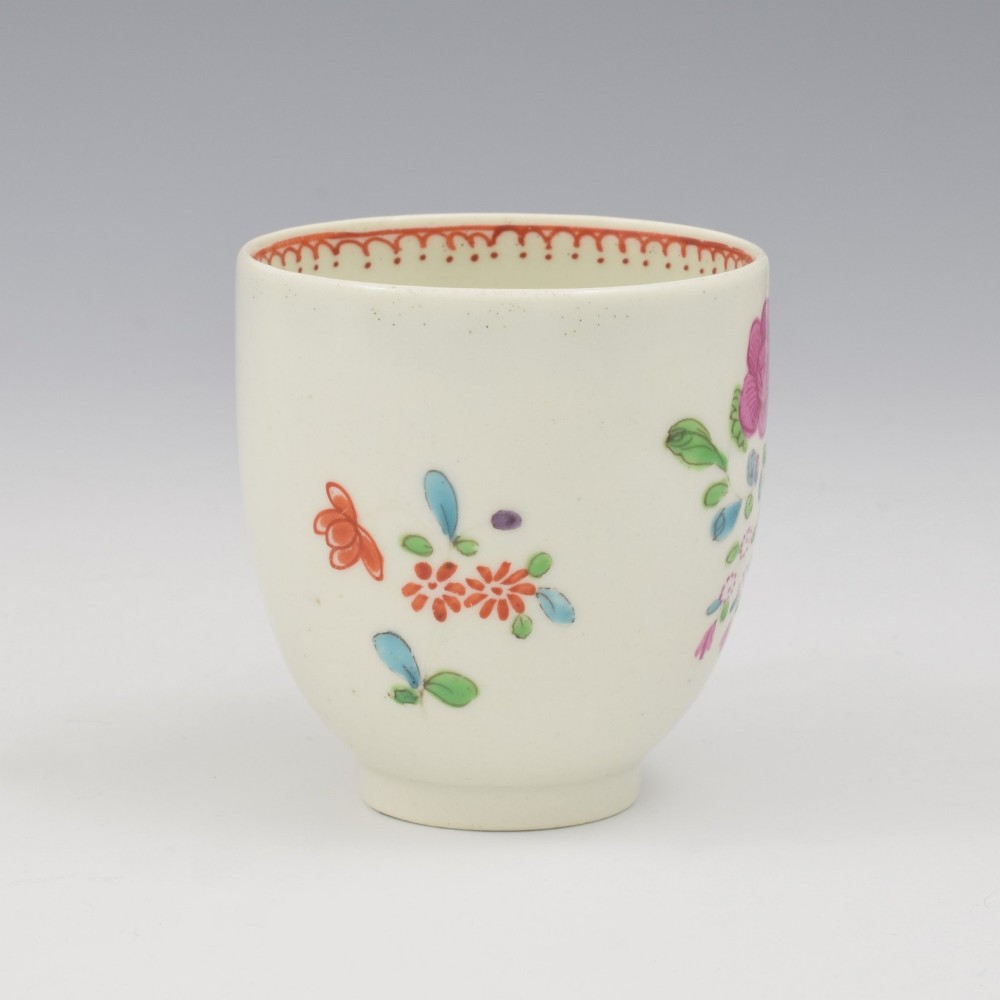 An 18th-century white porcelain coffee cup decorated with hand-painted polychrome floral sprays and an inner red patterned border. View II