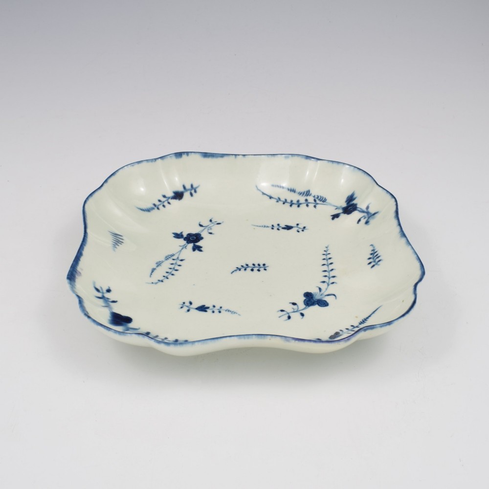 An 18th-century square lobed soft-paste porcelain dish decorated with hand-painted blue floral sprigs and a feathered rim. View II