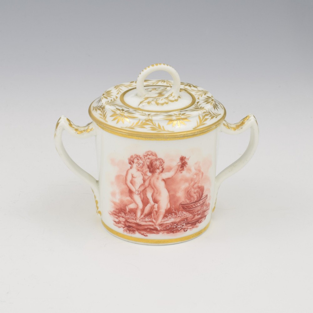 A white Regency period Bloor Derby porcelain chocolate cup featuring twin handles, a fitted lid with a loop finial, hand-painted sepia putti, and gold gilded leaf borders.