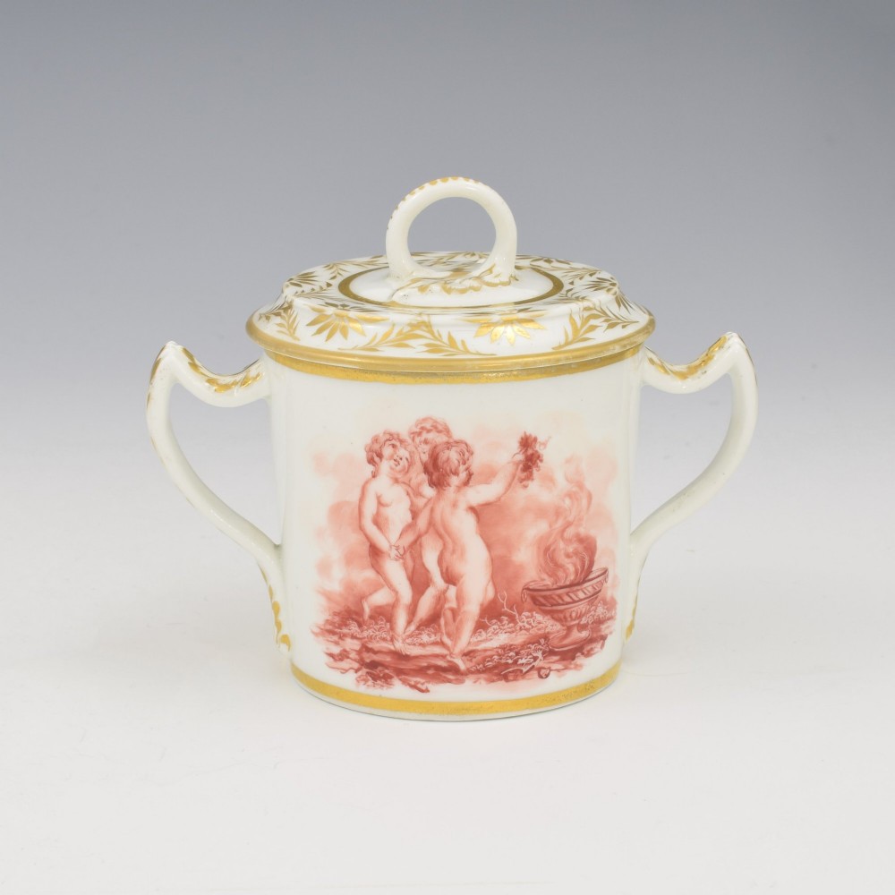 A white Regency period Bloor Derby porcelain chocolate cup featuring twin handles, a fitted lid with a loop finial, hand-painted sepia putti, and gold gilded leaf borders. View II